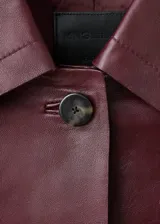 Chaqueta de cuero de corte recto con cuello camisero, cierre frontal de botones y dos bolsillos de parche con solapa en la parte delantera.