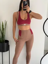 Conjunto deportivo de dos piezas compuesto por un top de escote redondo y calza larga de tiro alto. Ambas prendas presentan un diseño bicolor en tonos rojo y tostado, confeccionadas en tejido acanalado con detalles de costuras visibles.