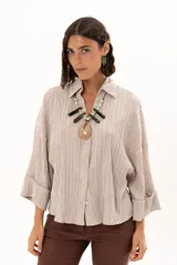 Camisa de textura plisada en color beige, con cuello clásico, cierre frontal de botones y mangas tres cuartos con puños vueltos.