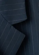 Blazer de doble botonadura color azul marino con estampado de raya diplomática, cuello en pico con solapa de muesca, bolsillos con solapa y diseño recto.