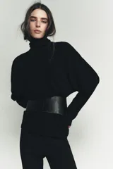 Jersey de punto liso color negro, con cuello subido y mangas largas de diseño murciélago con sisa ancha que se estrecha hacia la muñeca.