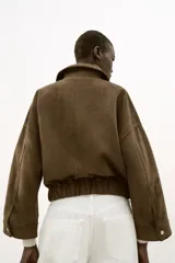 Cazadora de efecto ante con cuello solapa, cierre frontal con cremallera y mangas por debajo del codo. Presenta bolsillos delanteros de plastrón con solapa y bajo elástico.