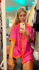 Camisola de lino fucsia con detalles en color naranja en cuello, solapa de botones, bordes de mangas y ruedo. De corte holgado, manga corta y cierre frontal con botones.