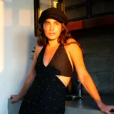 Vestido corto negro con estampado de plumas doradas, escote en V, breteles finos cruzados en la espalda, cut-outs laterales y volado en el ruedo.