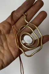 Collar con cordón marrón ajustable y dije dorado con forma de espiral irregular y centro de nácar.
