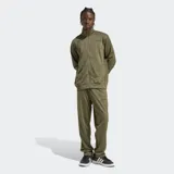 Conjunto deportivo Adidas compuesto por campera con cierre frontal y pantalón largo, ambos en color verde oliva. La campera presenta cuello alto y el pantalón cuenta con cintura elástica ajustable. Ambos incluyen bolsillos laterales y el logo de la marca estampado en tono oscuro.