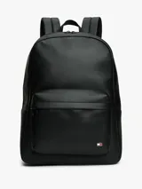 Mochila urbana de diseño minimalista confeccionada en poliuretano negro. Presenta un compartimento principal amplio con cierre, un bolsillo frontal con textura acanalada y el logo de la bandera de la marca en la esquina inferior. Incluye correas de hombro acolchadas y ajustables, además de un asa superior de mano.