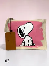 Sobre de cuero negro con textura granulada, intervenido a mano con una ilustración de Snoopy con anteojos y remera roja sobre un fondo pintado en rosa. Incluye etiqueta de cuero colgante con el logo de la colaboración.