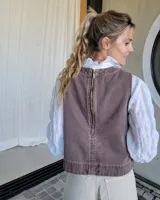 Chaleco de corte recto y largo a la cintura, confeccionado en denim con estampado de rayas verticales en tonos azul y blanco. Presenta cuello redondo y costuras visibles que definen su estructura.