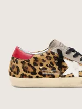Zapatilla de cuero vacuno con pelo de potro y estampado animal print, combinada con gamuza en la puntera y lengüeta. Presenta una estrella lateral de cuero blanco, detalle de cuero rojo en el talón, cordones oscuros y suela con efecto envejecido.