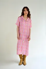 Vestido midi camisero con estampado a cuadros en tonos rosados y naranjas, con cuello clásico, mangas cortas y cierre frontal con botones.