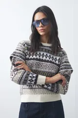 Sweater de punto con diseño jacquard de inspiración nórdica, cuello redondo y mangas largas. Presenta un patrón geométrico en tonos tierra, azul y blanco, con puños y ruedo acanalados.