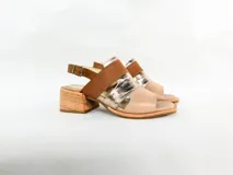 Sandalias de cuero color nude, con tiras cruzadas en dorado y marrón, taco de madera y pulsera al tobillo con hebilla.