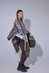 Ruana tejida en lana lambswool con diseño de bloques de color y tramas geométricas. Presenta cierre frontal con doble cursor y tiradores de cuero, permitiendo diferentes formas de uso.