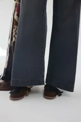 Pantalón jean gris oscuro de tiro medio y piernas anchas, con diseño de cinco bolsillos y cierre frontal con botón y cremallera.