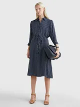 Vestido camisero midi azul marino con rayas verticales blancas, cuello camisero, cierre frontal con botones, mangas largas con puños abotonados y cinturón de lazo a juego.