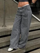 Pantalón de jean estilo wide leg, de tiro bajo, color gris lavado con efecto desgastado. Presenta corte recto y holgado en las piernas, con cierre frontal y bolsillos clásicos.