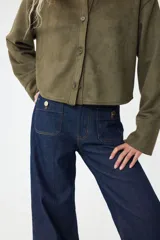 Camisa corta color verde militar, de corte holgado, con cuello clásico, botones frontales y canesú en la espalda. Presenta hombros caídos y mangas largas con puños anchos.