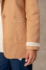 Blazer de lana soft color camel, con corte recto y solapas clásicas. Presenta detalles de encaje blanco en los puños y apliques de perlas en los bolsillos frontales.