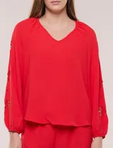 Blusa azul de corte holgado y fluido, con escote en V y mangas largas raglán que presentan detalles de calados con forma de flores y puños elastizados.