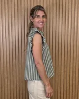 Musculosa a rayas verdes y blancas, con cuello alto fruncido, cierre frontal con botones y volados en los hombros.