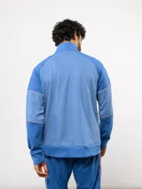 Buzo deportivo de medio cierre marca Umbro del Club Nacional de Football. Presenta un diseño en tonos azul y gris jaspeado, con cuello alto, mangas largas y detalles de costuras en contraste. Incluye el escudo del club y logo de la marca en el pecho.