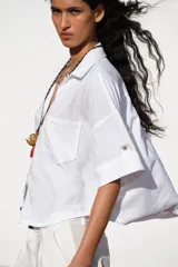 Camisa de lino color celeste claro, con cuello solapa, escote pico, manga corta con vuelta y dos bolsillos de plastrón en el delantero. Cierre frontal con botones.