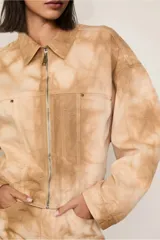 Chaqueta de algodón con estampado tie-dye en tonos beige y marrón claro, de corte recto, con cuello clásico, cierre frontal con cremallera, mangas largas y bolsillos frontales.