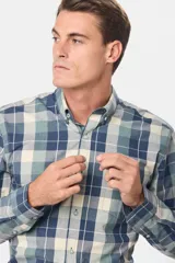 Camisa de manga larga con estampado de cuadros en tonos azules, grises y marrones. Presenta cuello abotonado, bolsillo frontal en el pecho y botones personalizados.