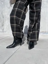 Pantalón de corte holgado y silueta tipo barrel, confeccionado en tela viyela con estampado de cuadrillé en tonos negro, beige y líneas finas rojizas. Presenta cintura elástica y puños ajustados en el tobillo.