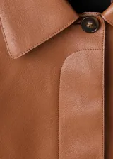 Chaqueta corta de efecto piel en color tostado, con cuello de solapa, cierre frontal de botones y dos bolsillos de parche con solapa en la parte delantera.