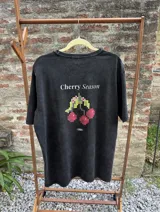Remera azul con efecto lavado, de corte holgado y manga corta. Estampa trasera con la frase "Cherry Season" y un diseño pixelado de cerezas.