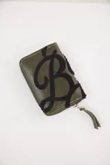 Billetera de cuero color verde oliva con cierre perimetral y detalle de letra B bordada en relieve con textura de felpa negra.