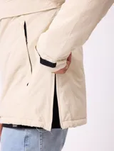 Campera tipo canguro Rusty, color beige, con capucha ajustable, cierre frontal parcial y bolsillo tipo sobre en el pecho con logo de la marca.