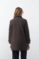 Tapado corto de paño color marrón, con diseño recto, cuello camisero y cierre frontal con broches metálicos. Cuenta con bolsillos frontales.
