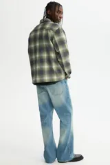 Sobrecamisa de franela suave con cuello inglés, bolsillos superiores con solapa y cierre frontal de botones. Presenta un diseño de cuadros en tonos verdes, grises y blancos, con mangas largas y bajo recto.