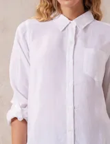 Camisa blanca de lino con cuello con solapa, manga larga regulable con presilla y botón, y abertura central con botones.