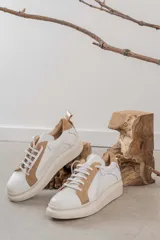 Championes de cuero con diseño de paneles en color blanco y tostado. Presentan suela de plataforma, cordones planos al tono y detalle de tirador en el talón.