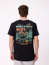 Remera de manga corta color crema con estampado gráfico en la espalda que representa un paisaje de montaña con un lago, árboles y una carpa, junto con el logo de la marca Rusty.