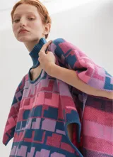 Poncho tejido con cuello alto y aberturas laterales, con diseño geométrico multicolor en tonos rosa, azul y violeta.