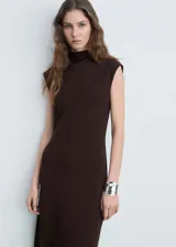 Vestido midi de color marrón chocolate, con cuello perkins, diseño sin mangas y corte evasé. Presenta un bajo asimétrico y cierre de botón en la parte posterior.