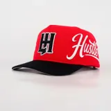 Gorro trucker rojo con visera negra, diseño estructurado, parche frontal con la letra H decorada con pedrería y texto bordado en el lateral.