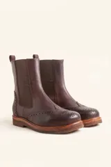 Bota tipo Chelsea de cuero vacuno color suela, con diseño brogue en la puntera y laterales. Presenta paneles elásticos laterales en color marrón oscuro, tirador trasero y suela de goma con plataforma.