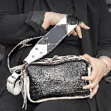 Bandolera negra con textura símil piel de cocodrilo, detalles en blanco y correa ancha ajustable con diseño geométrico en blanco y negro.