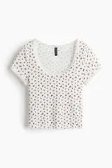 Top corto ajustado de manga corta en punto acanalado blanco con estampado flocado de flores rojas, escote redondo amplio y detalles de encaje con borde ondulado en el cuello, mangas y dobladillo.
