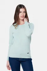 Buzo tejido en hilo de algodón color beige, con cuello redondo y manga larga. Presenta un corte clásico y un pequeño detalle metálico en la parte inferior izquierda.