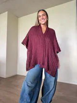 Ruana tejida de algodón con hilo lurex en punto jersey, color azul, con diseño amplio y detalle de etiqueta de cuerina en la parte posterior.