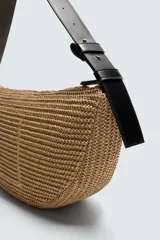 Bolso de hombro negro con acabado trenzado. Tiene un compartimento principal con cierre de cremallera y un bolsillo plano en el interior. El asa de hombro es ajustable.