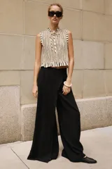 Pantalón negro de tiro alto con diseño cruzado tipo pareo, pinzas delanteras y pernera ancha. Cuenta con cierre lateral de cremallera oculta.