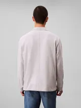 Chomba de manga larga Calvin Klein color gris, confeccionada en tejido jersey grueso aterciopelado de algodón. Cuenta con cuello clásico, cierre frontal con tres botones y logo de la marca bordado en relieve en el pecho.